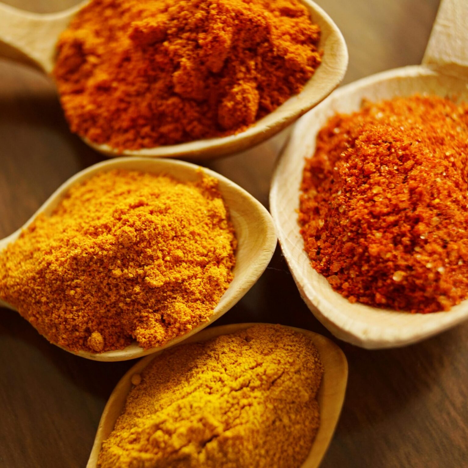 Close-up of vibrant spices like turmeric and chili powder in wooden spoons.