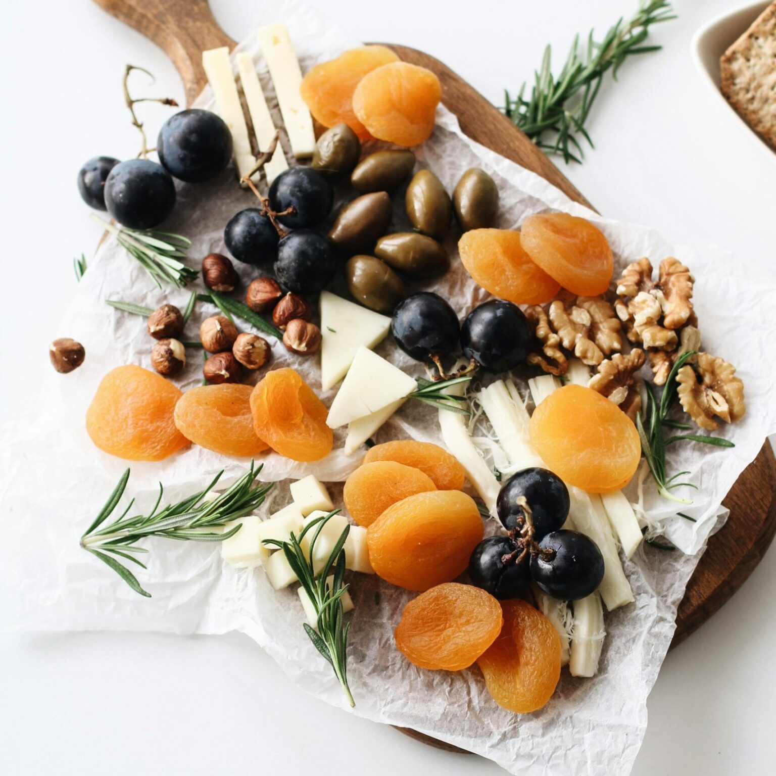 A rustic cheese platter with assorted nuts, dried fruits, and olives on a wooden board.