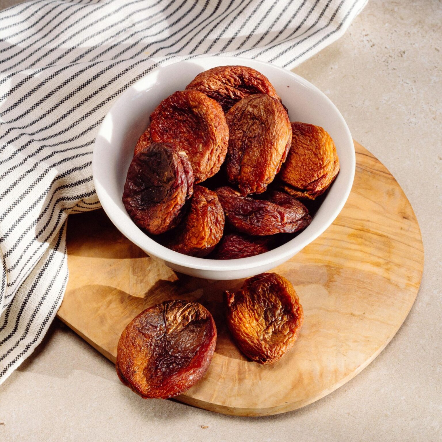 A bowl of dried apricots on a wooden board in warm sunlight, perfect for food blogging.