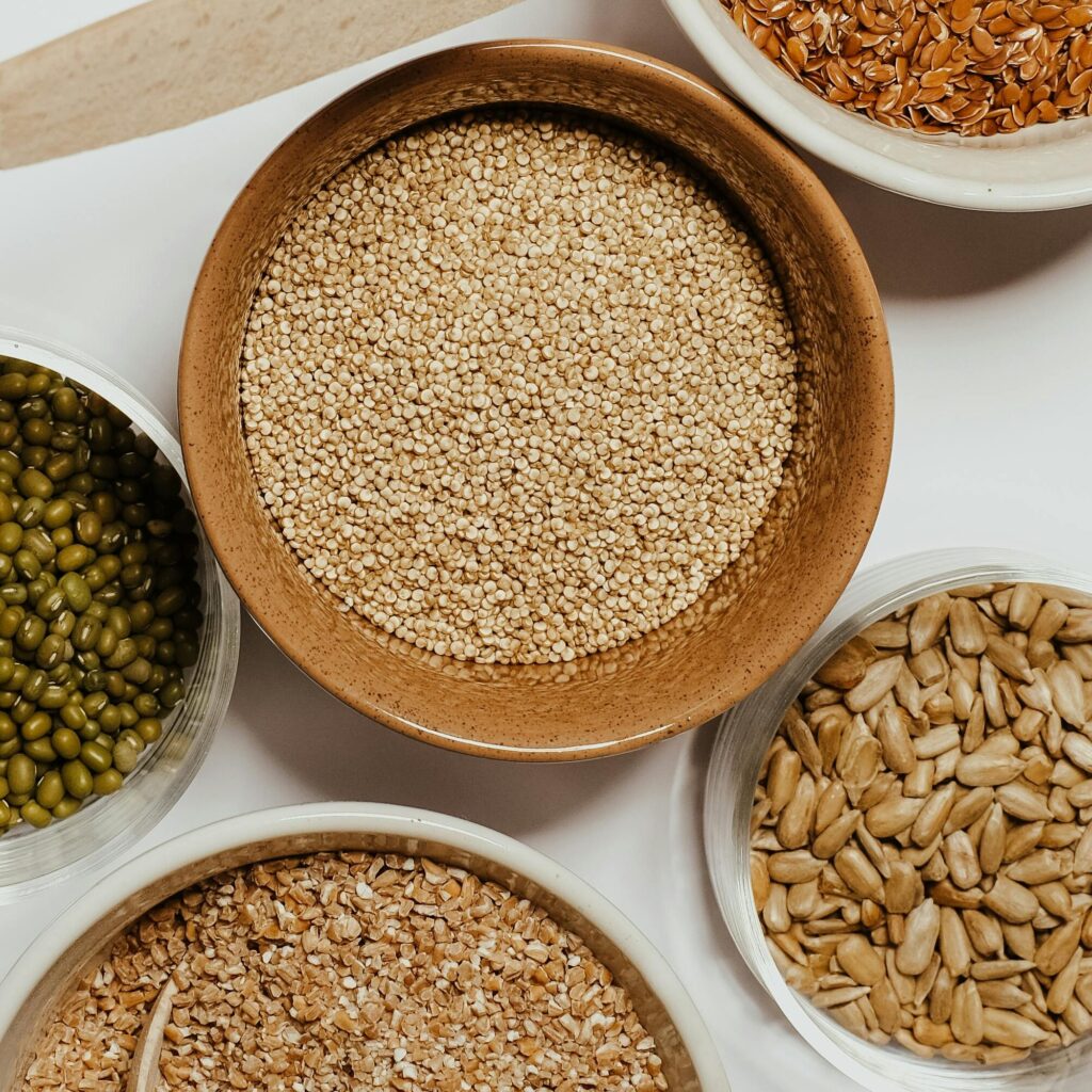 Top view of assorted grains in bowls with wooden spoons on a minimalist background.